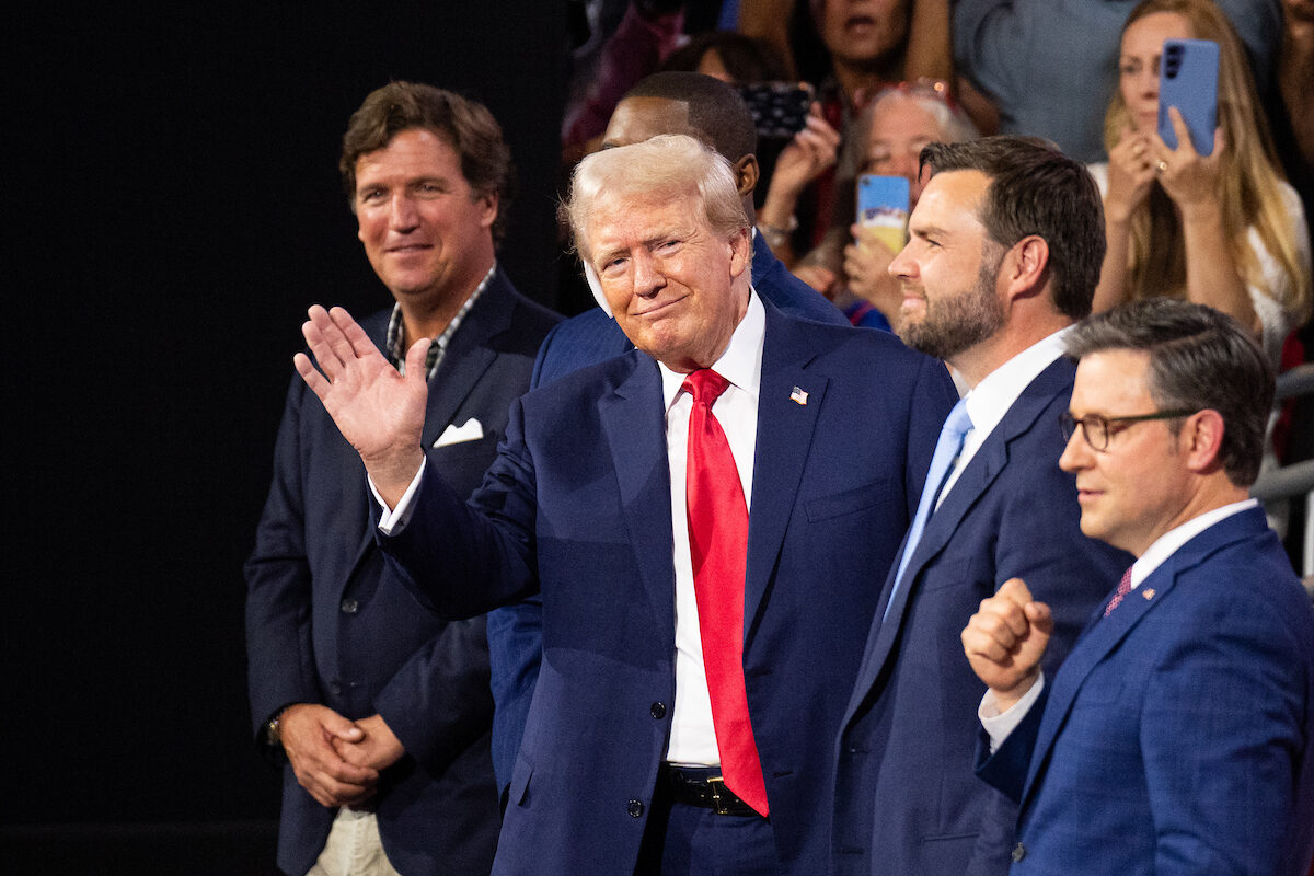 Former President Donald Trump waves to the crowd at the Republican National Convention at the Fiserv Forum in Milwaukee on Monday. Trump is flanked from left by Tucker Carlson, Rep. Byron Donalds, R-Fla., vice presidential nominee Sen. J.D. Vance, R-Ohio, and Speaker Mike Johnson, R-La.