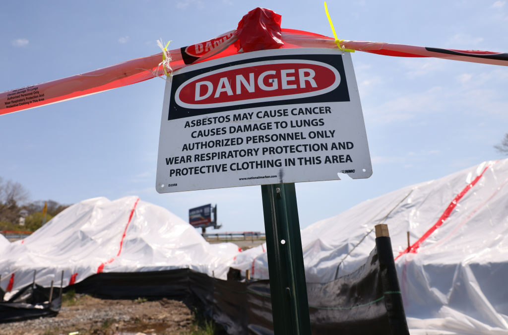 A sign warning people of asbestos is seen in front of a pile of construction debris that was dumped on a highway near a development in Chelsea, Mass., on May 5, 2022. 