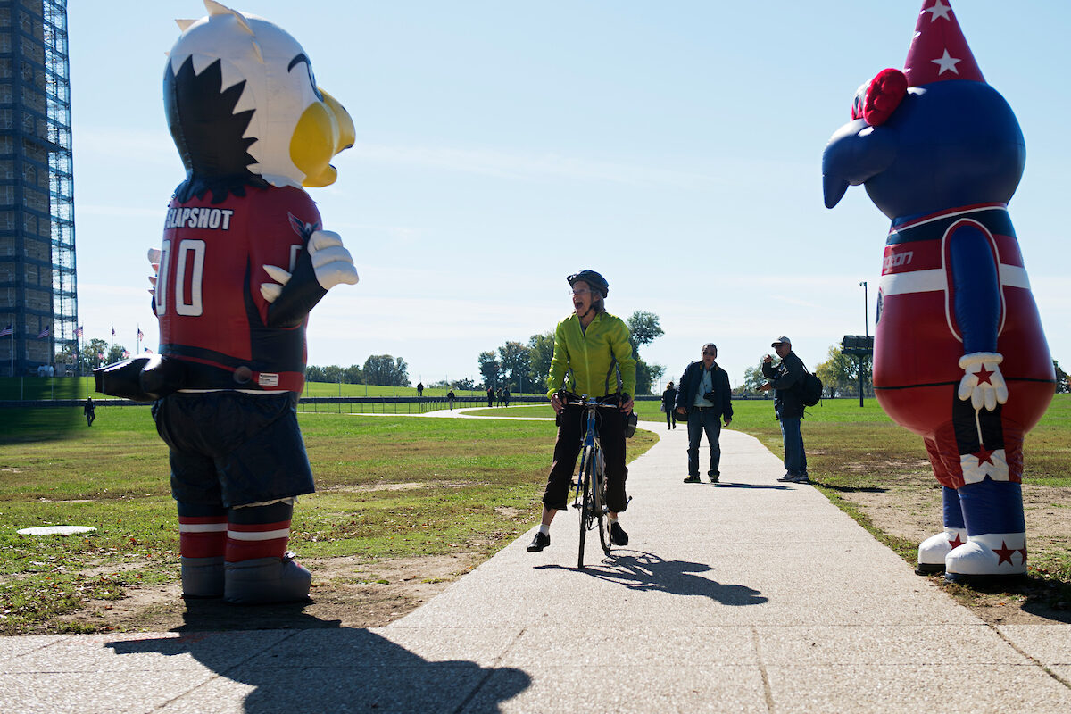 Mascots for the Washington Capitals, left, and Wizards, surprise a biker on the Mall as the duo was being filmed. The two teams are looking to move to Virginia and away from downtown DC after more than 25 years. 